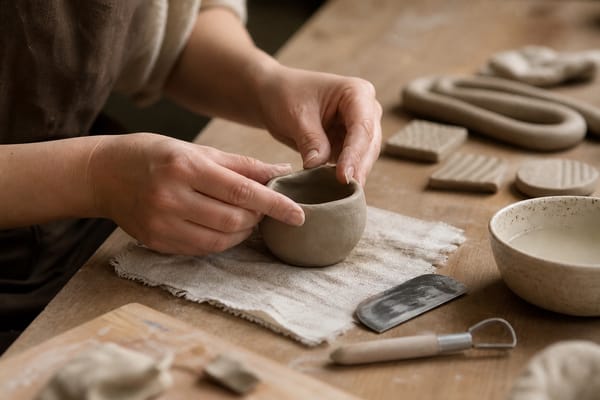Hands shaping a small clay pinch pot in a beginner pottery studio